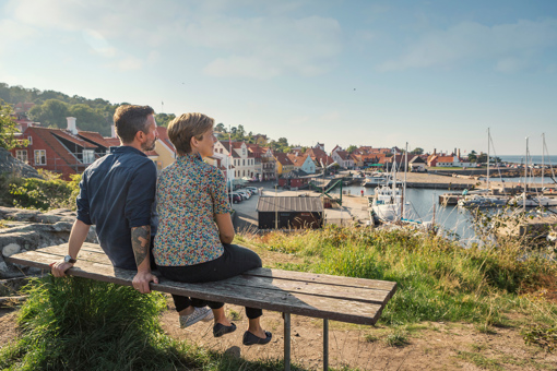 Ein paar genießt auf einer Bank den Ausblick auf den Hafen von Gudhjem