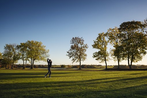Ein Mann schwingt seinen Golfschläger auf Bornholm vor blauem Himmel