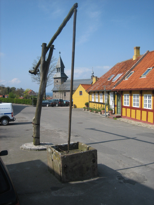 Ein alter Schwenkbrunnen in Gudhjem vor der Kirche und alten farbenfrohen Fachwerkhäusern