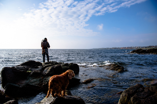 Angler steht mit seinem Hund auf den Felsen an der Nordküste von Bornholm