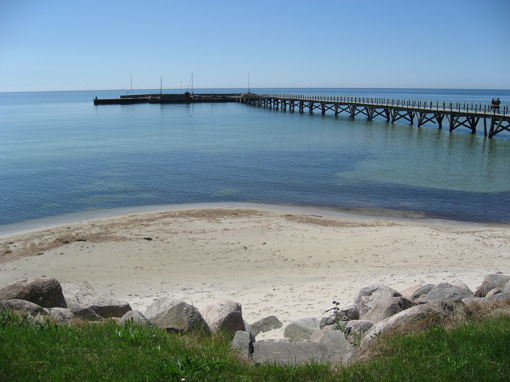 Blick über den Strand auf den langen Holzsteg von Arnager