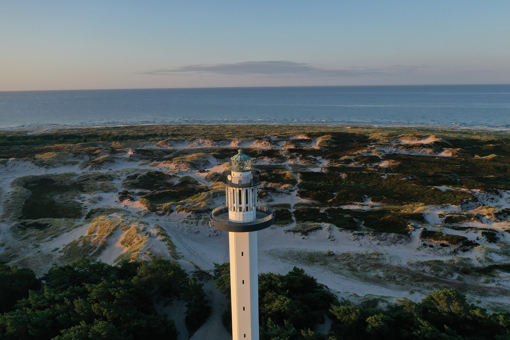 Der hohe, weiße Leuchtturm Dueodde Fyr mit Dünen und Ostsee im Hintergrund