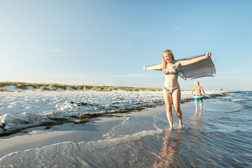 Junge und Mädchen in Badekleidung genießen den Aufenthalt an der Wasserkante am Dueodde Strand