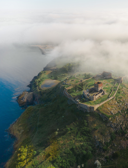 Luftaufnahme der in Wolken getauchten Burgruine Hammershus mitsamt der Felsenküste Nordbornholms