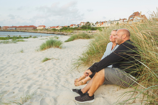 Ein Paar sitzt umgeben von Strandhafer am Sandstrand bei Nørrekaas und genießt das Abendlicht und die Aussicht 