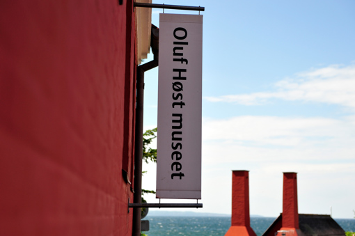 Das Schild des Oluf Høst Museums an der roten Hausfassade im Herzen von Gudhjem